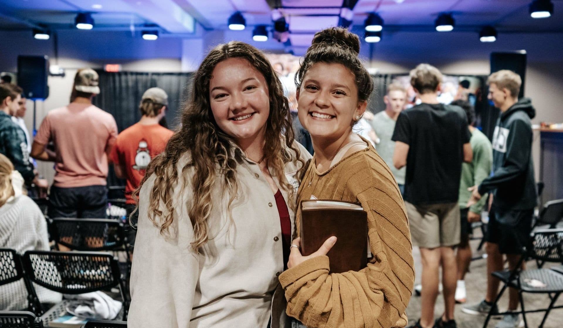 Two students smiling together after a gathering, one holding a Bible